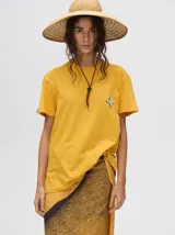 Remera de corte cuadrado y ajuste holgado, color verde oliva, con pequeño estampado gráfico de un velero en el pecho y etiqueta decorativa en la manga.