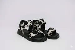 Sandalias bajas con suela negra y tiras de cuero con estampado de vaca.