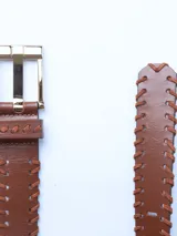 Cinturón marrón de cuero con costuras gruesas en contraste y hebilla metálica dorada.