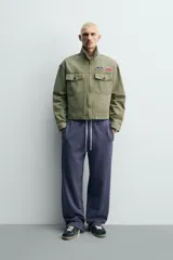 Cazadora cropped de algodón con efecto lavado, color verde militar. Presenta cuello solapa, cierre frontal con cremallera, bolsillos frontales de plastrón con solapa y parches decorativos en el pecho.