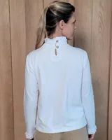 Polera de manga larga color blanco, confeccionada en algodón, con cuello alto tipo tortuga y detalles de volados en el cuello y en los puños.