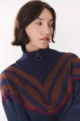 Buzo de tejido de punto en color azul marino, con cuello alto y cierre frontal parcial. Presenta un diseño con franjas en color marrón y detalles de líneas en rojo en el pecho, hombros y ruedo. Tiene corte holgado y mangas largas con puños acanalados.