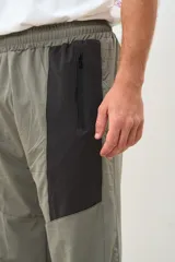 Pantalón deportivo gris con paneles laterales negros, cintura elástica y puños ajustados.