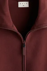 Buzo deportivo de polar color bordó, con cuello alto y cierre frontal parcial. Presenta mangas largas de corte caído y bolsillos laterales integrados en la costura.
