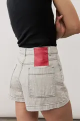 Short gris claro de tiro alto con costuras pespunteadas en contraste y bolsillos traseros amplios. Presenta una etiqueta de cuero rojo en la parte posterior de la cintura.