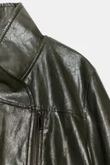 Chaqueta de corte amplio estilo biker en tejido efecto piel de color verde oscuro, con cuello alto envolvente, cierre frontal asimétrico de cremallera metálica, bolsillos ocultos en costura y forro interior.