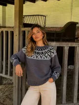 Buzo de lana merino con diseño jacquard en el canesú y los puños, combinando tonos gris, negro y crudo. Presenta cuello redondo y puños acanalados.