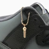 Championes Nike Dunk High de corte alto, con diseño en combinación de cuero negro y gris. Presenta suela de goma en tono crema envejecido y detalle de dije metálico colgante en el cuello.