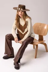 Sweater de punto color crema con cuello medio alto y silueta relajada. Presenta un diseño frontal con líneas en V decoradas con flecos largos de color marrón aplicados a mano.