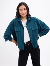 Campera de pana negra con cierre frontal de botones metálicos, cuello clásico y dos bolsillos frontales con solapa. Presenta mangas largas con puños abotonados y un diseño liviano sin forro.