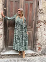 Vestido largo de corte holgado con estampado botánico y geométrico en tonos verdes y blancos. Presenta escote en V con cordones, mangas largas abullonadas con puños elásticos y falda con vuelo.