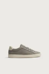Zapatilla deportiva para hombre fabricada en piel con acabado en serraje, color gris. Presenta diseño liso con detalle de contraste en el talón en tono claro y suela de goma con volumen.
