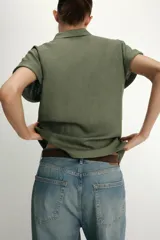 Camisa blanca confeccionada en tejido con lino, con cuello solapa y manga muy corta con terminación en vuelta. Presenta un detalle de nudo en el delantero y cierre frontal con botones metálicos.