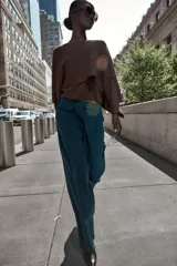 Pantalón de vestir marrón oscuro, tiro alto, con pernera ancha y pinzas frontales. Presenta un bolsillo con tapeta en la parte superior delantera.