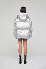 Campera puffer de corte holgado y acabado metalizado, con cuello alto envolvente, capucha desmontable y cierre frontal con botones. Presenta mangas amplias y bolsillos frontales con solapa.