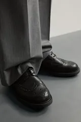 Zapato de vestir tipo brogue negro, con detalles de perforaciones decorativas y suela track dentada.