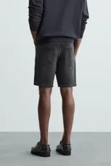 Bermuda de denim de algodón con elasticidad, color negro lavado. Modelo de tiro medio con corte regular fit, cinco bolsillos y cierre frontal con cremallera y botón.