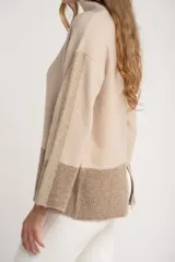 Sweater tipo polera de calce oversize, con diseño color block que combina tonos beige y marrón. Presenta cuello alto, mangas largas con puños acanalados y un panel inferior acanalado a juego.