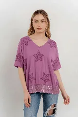Blusa lila de algodón con escote en V, mangas cortas y holgadas. Presenta estrellas bordadas en relieve en la parte superior y un borde de lentejuelas en el dobladillo inferior.