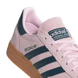 Championes adidas modelo Handball Spezial, confeccionados en gamuza color rosado con las icónicas tres tiras y detalle en el talón en color azul oscuro. Presentan una suela de goma color caramelo que aporta un estilo retro y distintivo.
