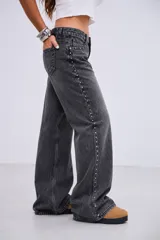 Pantalón de denim tiro bajo, color gris lavado, de corte recto y holgado. Presenta una línea de tachas metálicas pequeñas a lo largo de la costura lateral externa.