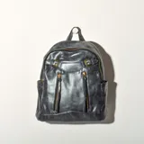 Mochila gris de cuero sintético con herrajes dorados. Tiene un compartimento principal con cierre, dos bolsillos frontales con cierre y bolsillos laterales abiertos.