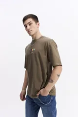 Remera de manga corta color verde militar, con escote redondo y un pequeño estampado frontal de formas geométricas de colores y texto manuscrito.