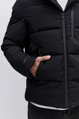 Cazadora acolchada negra con capucha, cierre frontal con cremallera y diseño de paneles horizontales. Presenta un parche decorativo en la manga y un ajuste cómodo.