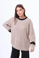 Buzo tejido de punto en color beige, con cuello redondo, puños y ruedo acanalados. Presenta detalles de rayas horizontales en color negro en el cuello y en los puños.