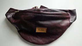 Riñonera de cuero color negro, de diseño suave y abombado, con cierre superior y etiqueta frontal con el logo de la marca.