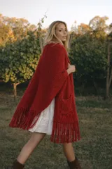 Ruana de lana merino color bordó, con diseño tejido de punto, bolsillos frontales aplicados y terminación con flecos en el ruedo.