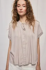 Camisa de manga corta color celeste, confeccionada en viscosa fluida, con silueta amplia y escote redondo con frunces y lazo para anudar.