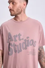 Remera manga corta oversize color rosa con estampa frontal con la leyenda "Art Studios" en gris.