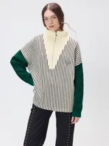 Pullover de tejido acanalado grueso con cuello alto y cierre frontal parcial. Presenta un diseño de bloques de color, con cuerpo en tono beige y mangas en contraste con rayas verticales en tonos rojizos. Incluye un detalle bordado en el pecho.