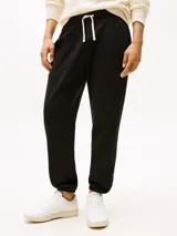 Pantalón de jogging negro de corte regular, confeccionado en felpa aterciopelada de mezcla de algodón y poliéster. Presenta cintura con cordón, bolsillos laterales y trasero, y bajos elásticos. Incluye logo de Tommy Hilfiger bordado en el muslo.