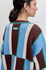 Cardigan de punto con diseño de bloques de color en azul, rojo y crema. Presenta cuello en V, cierre frontal con botones, mangas largas y dos bolsillos delanteros con bordado de cerezas.