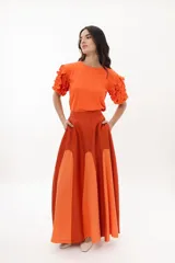 Falda larga de corte acampanado con diseño color block en tonos naranja y terracota. Presenta una caída fluida, bolsillos laterales y cierre lateral.