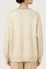 Cardigan de punto color beige jaspeado, con escote en V, cierre frontal de botones y detalles bordados decorativos en el escote y alrededor de los botones.