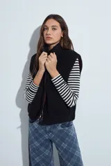Chaleco de corderito negro con textura suave, cuello alto y cierre frontal completo. Cuenta con bolsillos laterales amplios y un diseño de calce relajado.