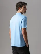 Chomba de manga corta Calvin Klein confeccionada en algodón interlock, con cuello clásico y cierre frontal de botones. Presenta un diseño liso en color celeste con el logo de la marca bordado sutilmente en el pecho.