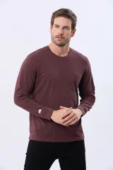 Remera de manga larga con cuello redondo, confeccionada en tejido de algodón con textura jaspeada. Presenta un pequeño logo bordado en el pecho y una etiqueta decorativa en el puño.