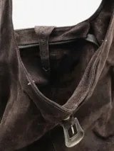 Cartera tipo hobo de diseño amplio y estructura flexible, confeccionada en gamuza color marrón con acabado desgastado. Cuenta con un asa única para llevar al hombro y un cierre frontal con detalle de hebilla metálica decorativa.