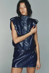 Falda mini de tiro bajo color azul marino, con efecto piel. Presenta una cintura con trabillas y un cinturón ajustable con botones a presión y tachas plateadas a contraste. Tiene forro interior a tono y cierre lateral con cremallera oculta.