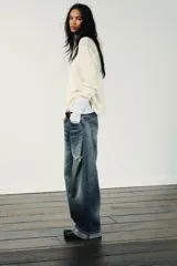 Jeans de mezclilla azul con lavado desgastado y rotos en la pierna derecha. Tienen tiro medio, corte ancho (baggy) y puños doblados en el bajo.