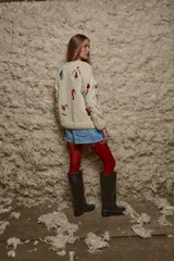 Sweater de lana color crema, tejido a mano con cuello redondo y mangas largas con trenzas. Presenta bordados de figuras esquiando en varios colores.