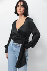 Camisa tipo blusa cruzada de seda negra, con escote en V profundo, mangas largas con puños abotonados y lazo lateral para anudar en la cintura.