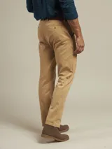 Pantalón de vestir color beige, de corte recto, con bolsillos laterales y traseros. Se ajusta a la cintura con cinturón de cuero marrón.