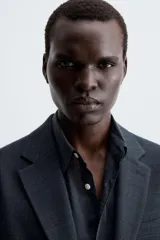 Blazer slim fit de color gris, confeccionada en tejido con lana. Presenta cuello con solapas de muesca, cierre frontal con un botón, bolsillos de solapa en la cadera y bolsillo de vivo en el pecho.