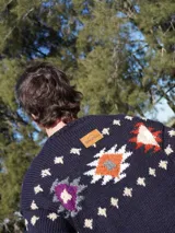 Sweater de lana azul marino con cuello redondo y diseño de copos de nieve y flores en tonos blanco, rojo y violeta. Tejido a mano.