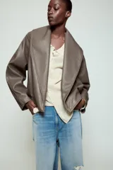 Cazadora Zara Woman Collection de efecto piel con cuello solapa ancho, manga larga, bolsillos delanteros y bajo elástico. Presenta un cierre frontal cruzado con botón a presión.